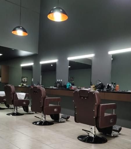 Cadeiras de barbeiro sob luminárias âmbar no salão da Menegatti